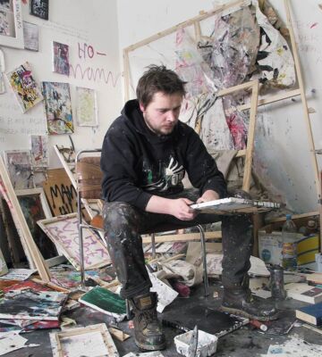 Portrait eines Künstlers sitzend zwischen seinen Malereien